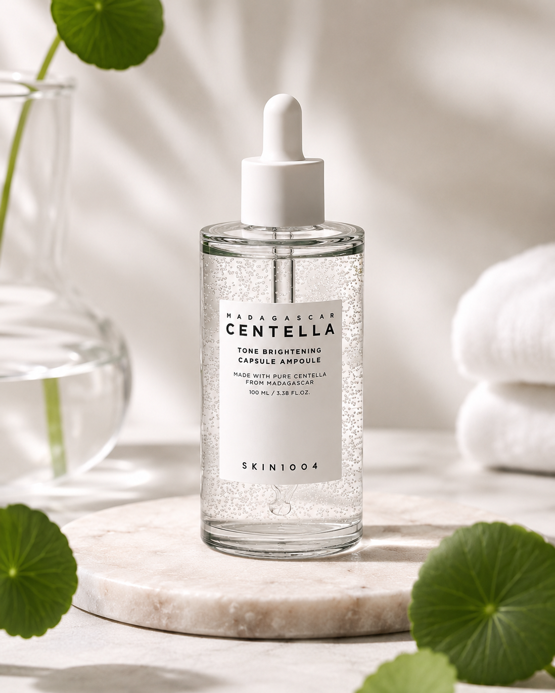 SKIN1004 Madagascar Centella Tone Brightening Capsule Ampoule 100ml on a marble surface with green leaves and towels in the background