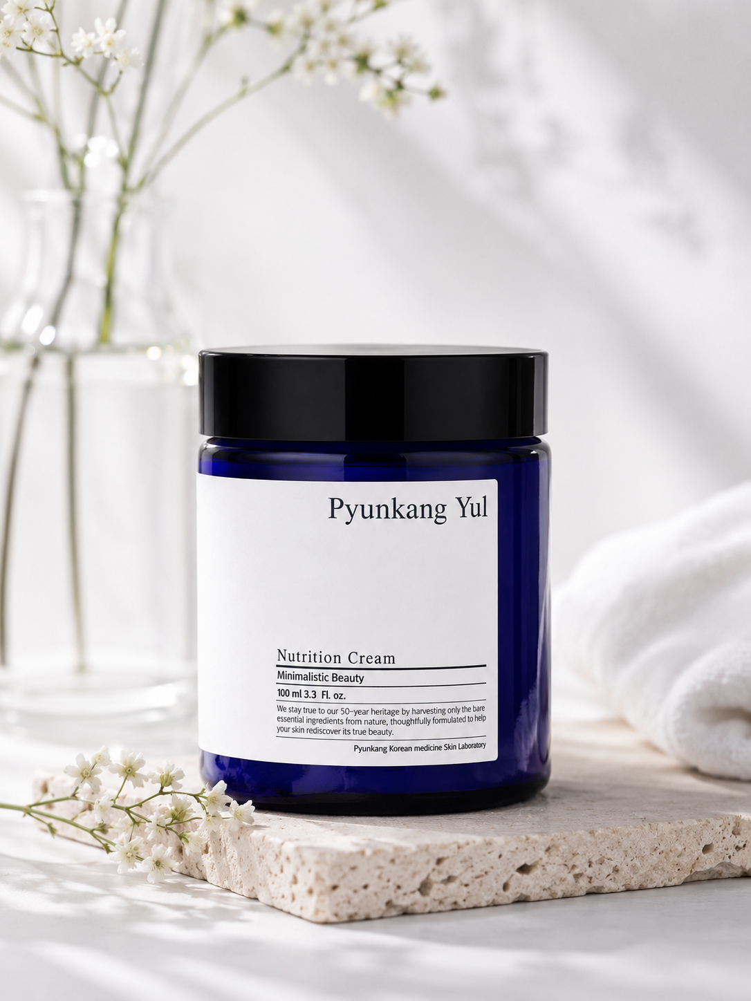 Pyunkang Yul Moisture Cream 100ml jar on a white surface with white flowers and a towel in the background