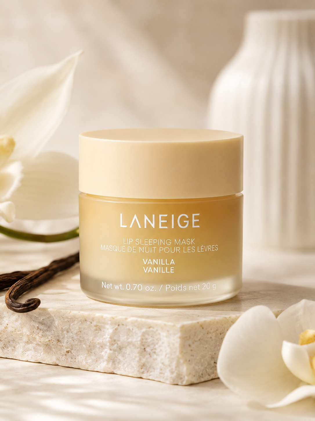 A jar of Laneige Lip Sleeping Mask EX Vanilla sits on a marble surface, surrounded by vanilla pods and white flowers, highlighting its luxurious packaging and nourishing formula.